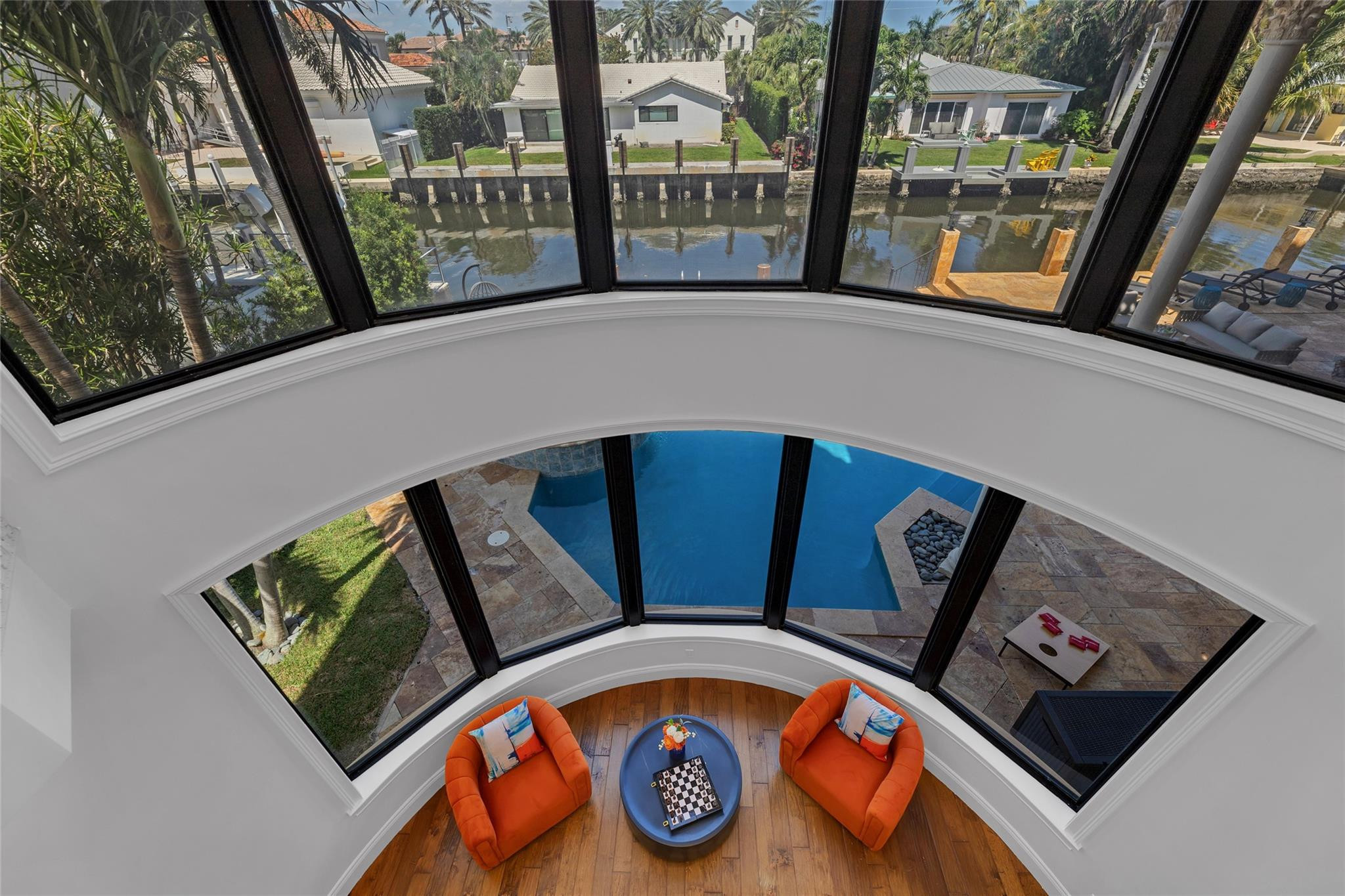 Curved sitting area with orange chairs overlooking a pool and canal through expansive windows.
