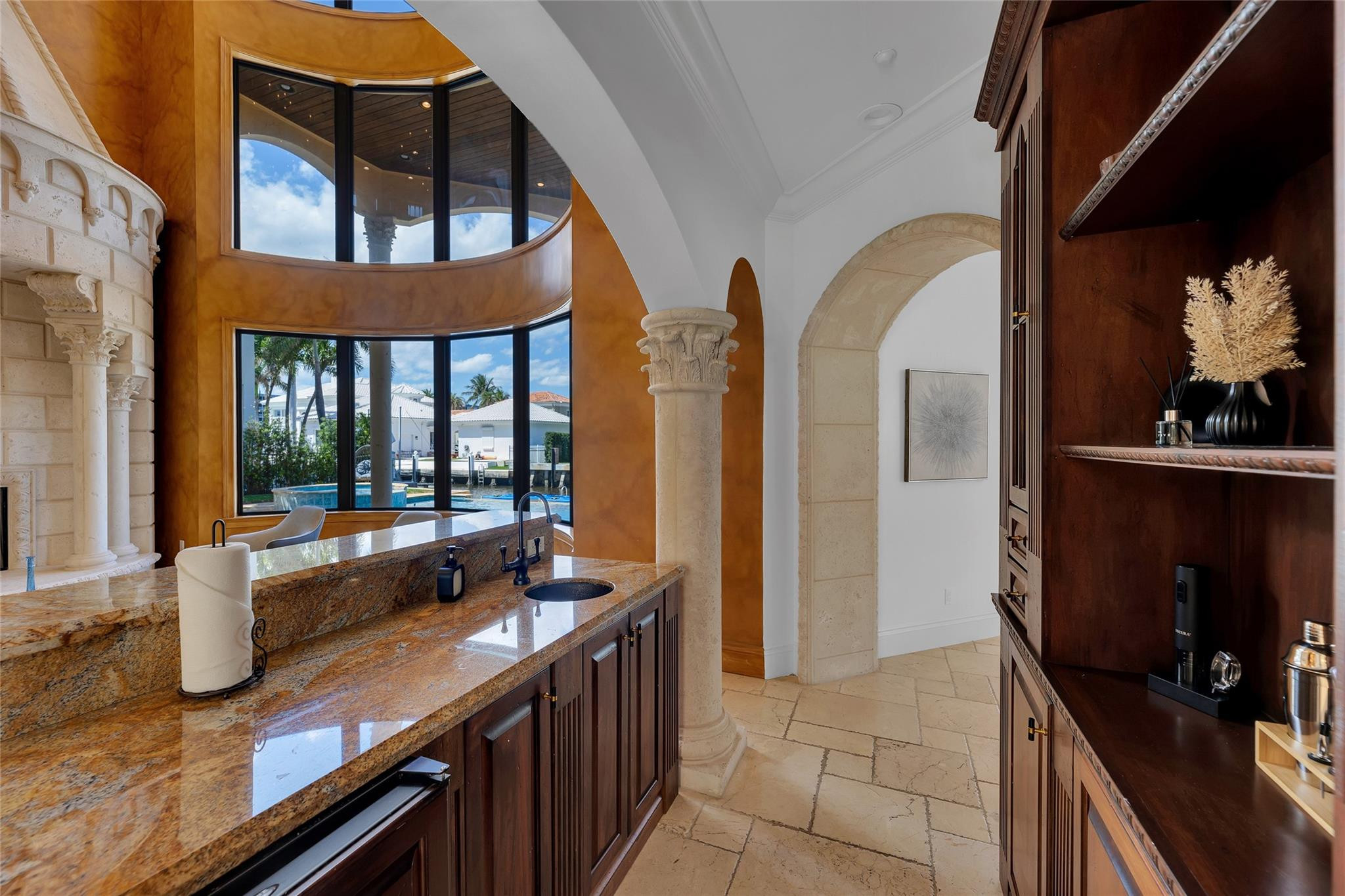 Home bar with granite counters and curved windows overlooking a pool and waterfront homes.