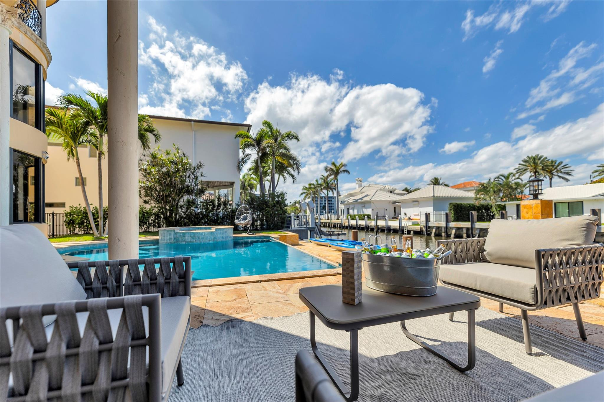 Waterfront patio with a pool and raised spa, furnished with lounge seating overlooking a palm-lined canal.