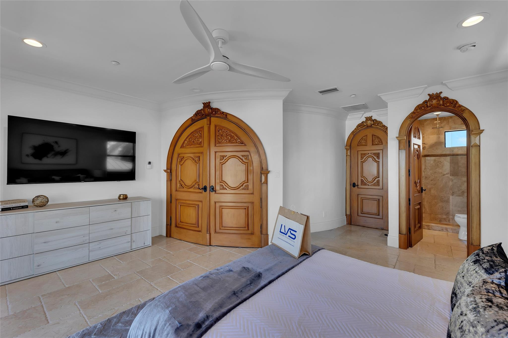 Furnished bedroom with ornate arched wooden doors and an open doorway to a tiled bathroom.