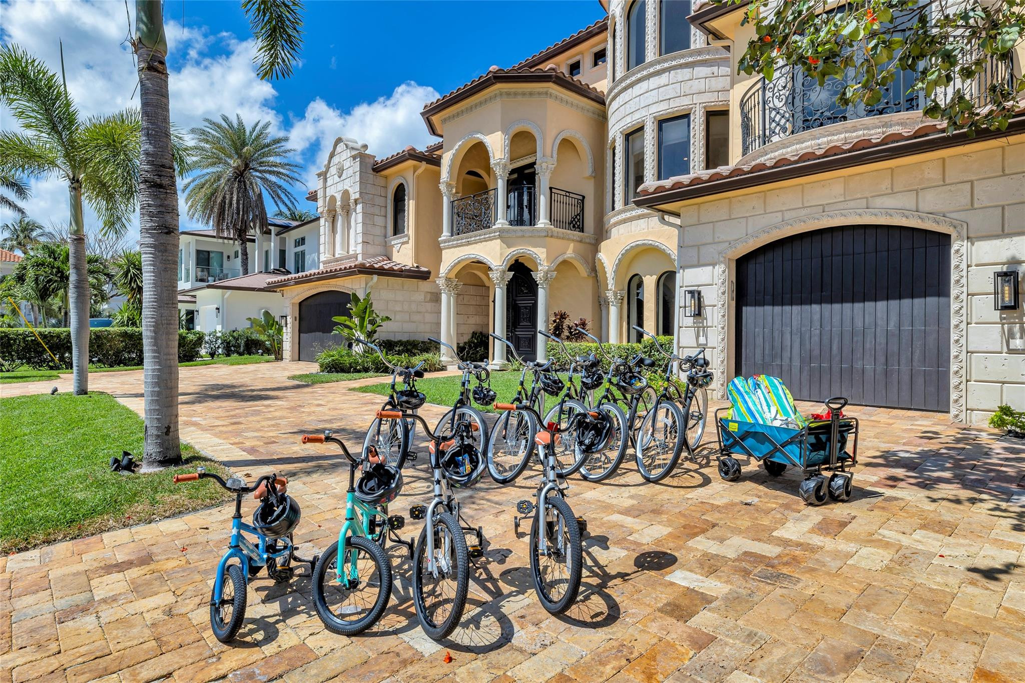Mediterranean-style home with arched balconies, a stone facade, palm trees, and bicycles on the driveway.