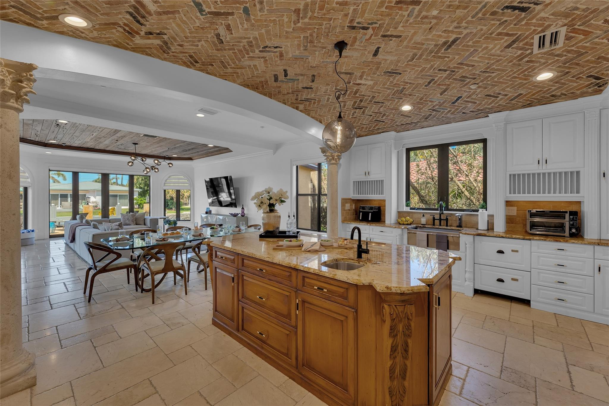 Kitchen with a carved wood island, white cabinetry, and exposed brick ceiling opening to dining and living areas.