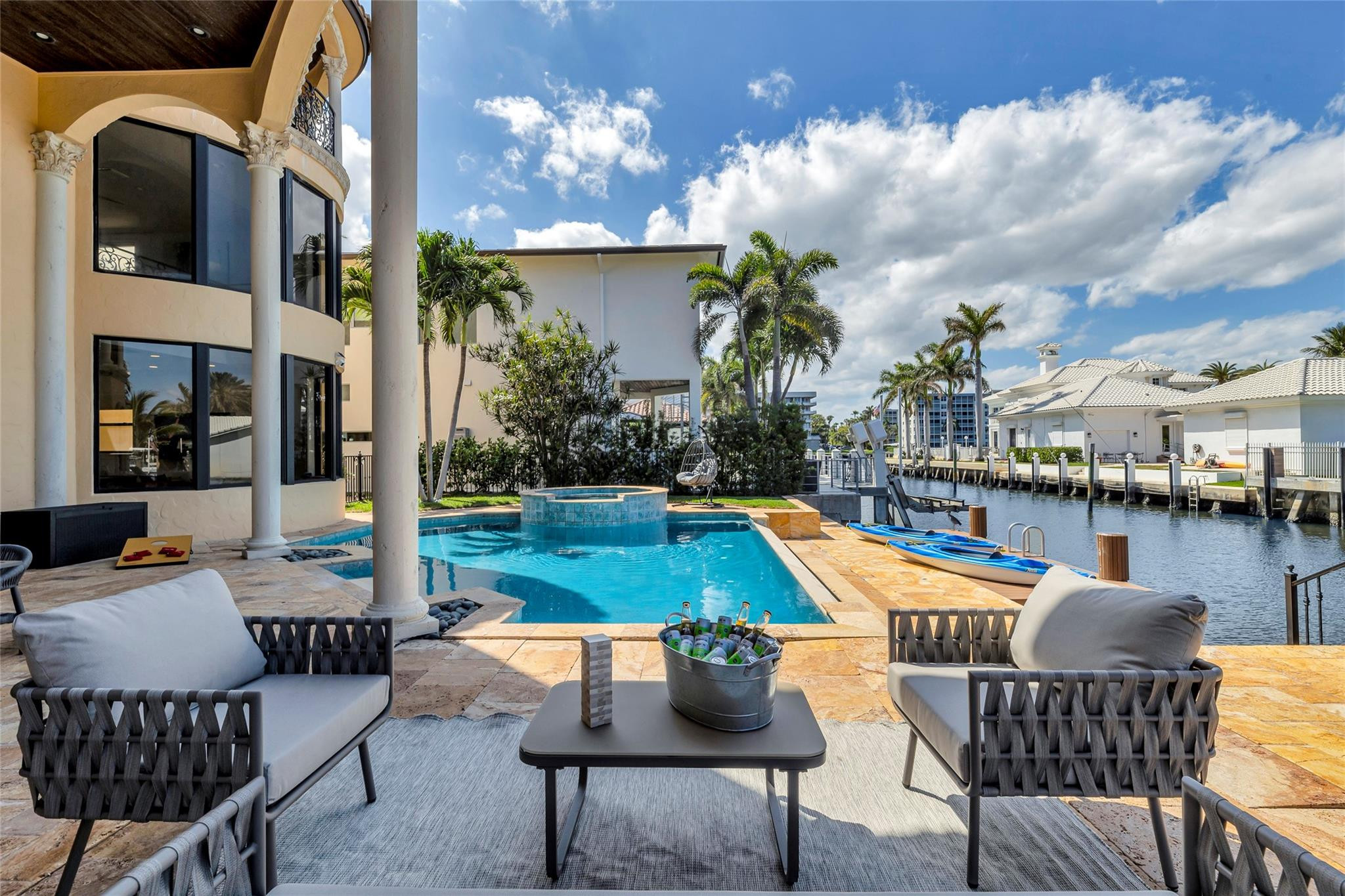 Waterfront pool and raised spa beside a canal, with furnished patio seating and kayaks on the dock.