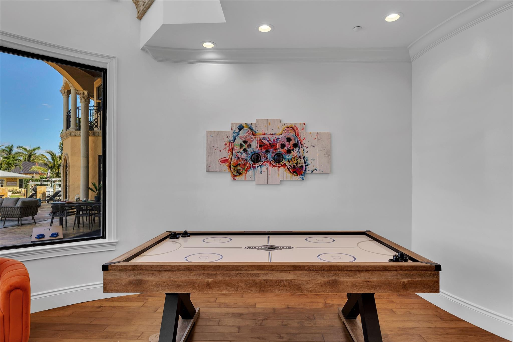 Game room with a wooden air hockey table and colorful controller artwork, opening onto a patio.