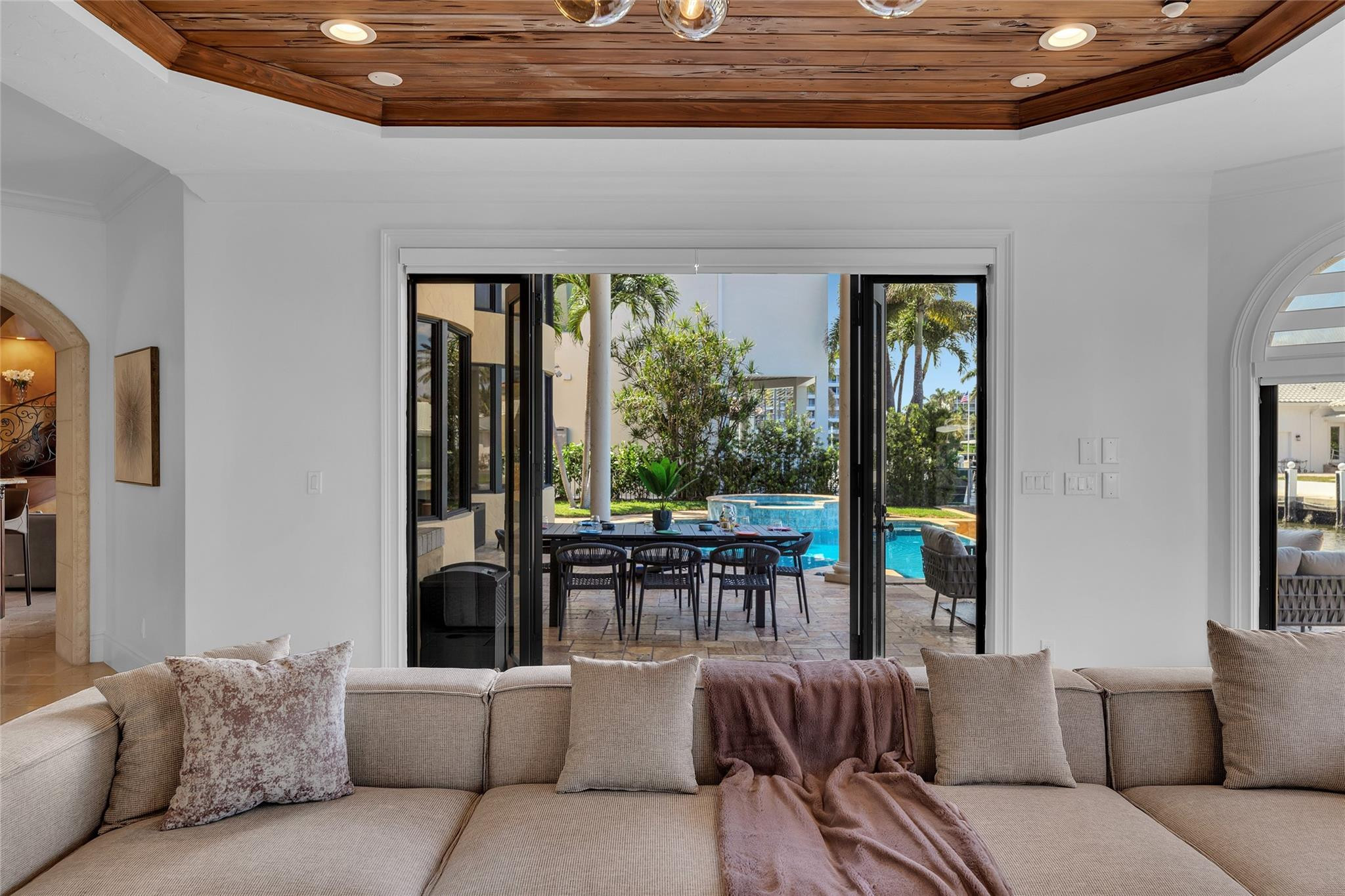 Living room with a wood-plank ceiling and sectional sofa overlooking a patio and swimming pool.