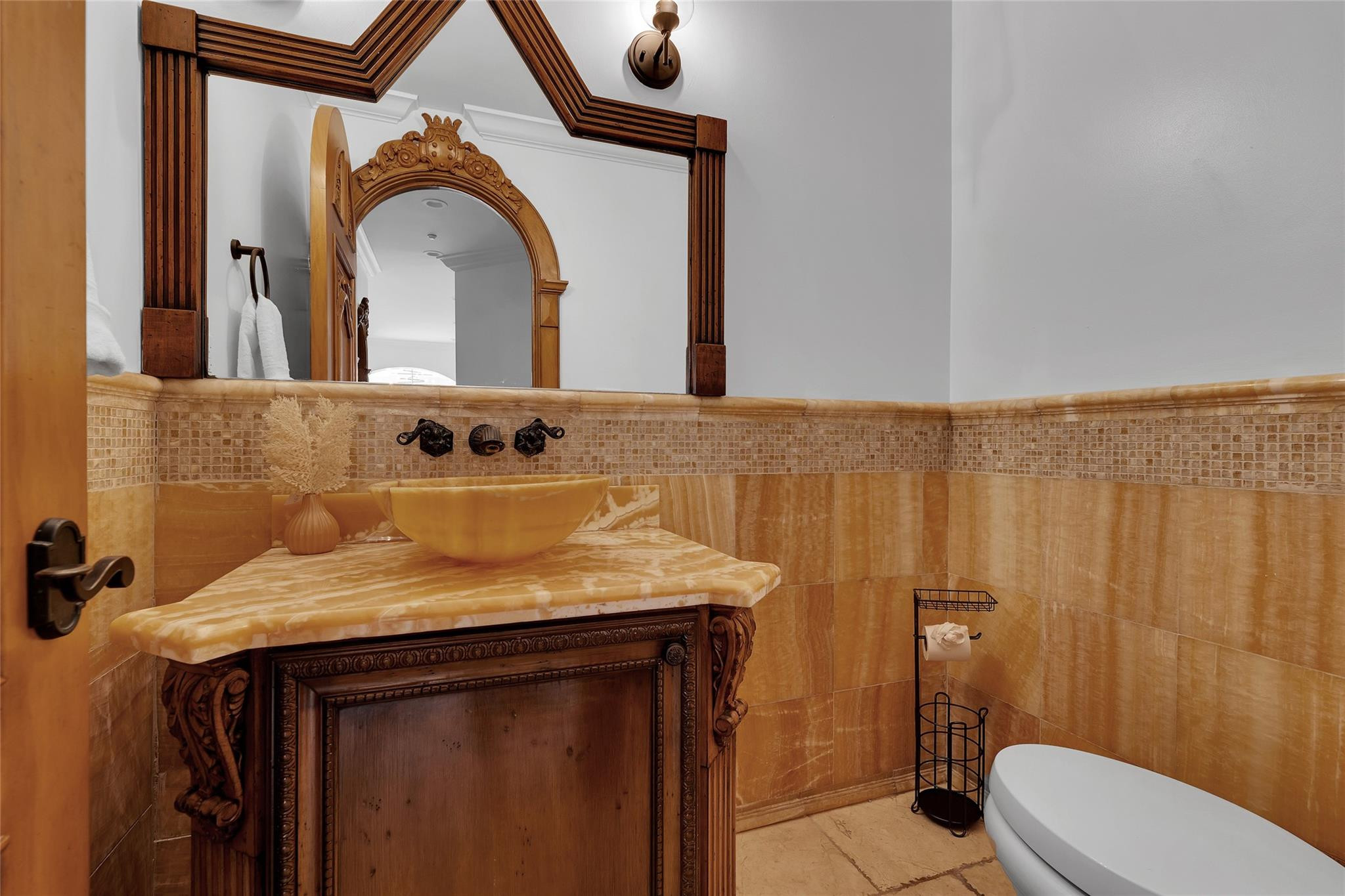 Bathroom with an ornate carved wood vanity, amber stone tile, and a white bathtub.