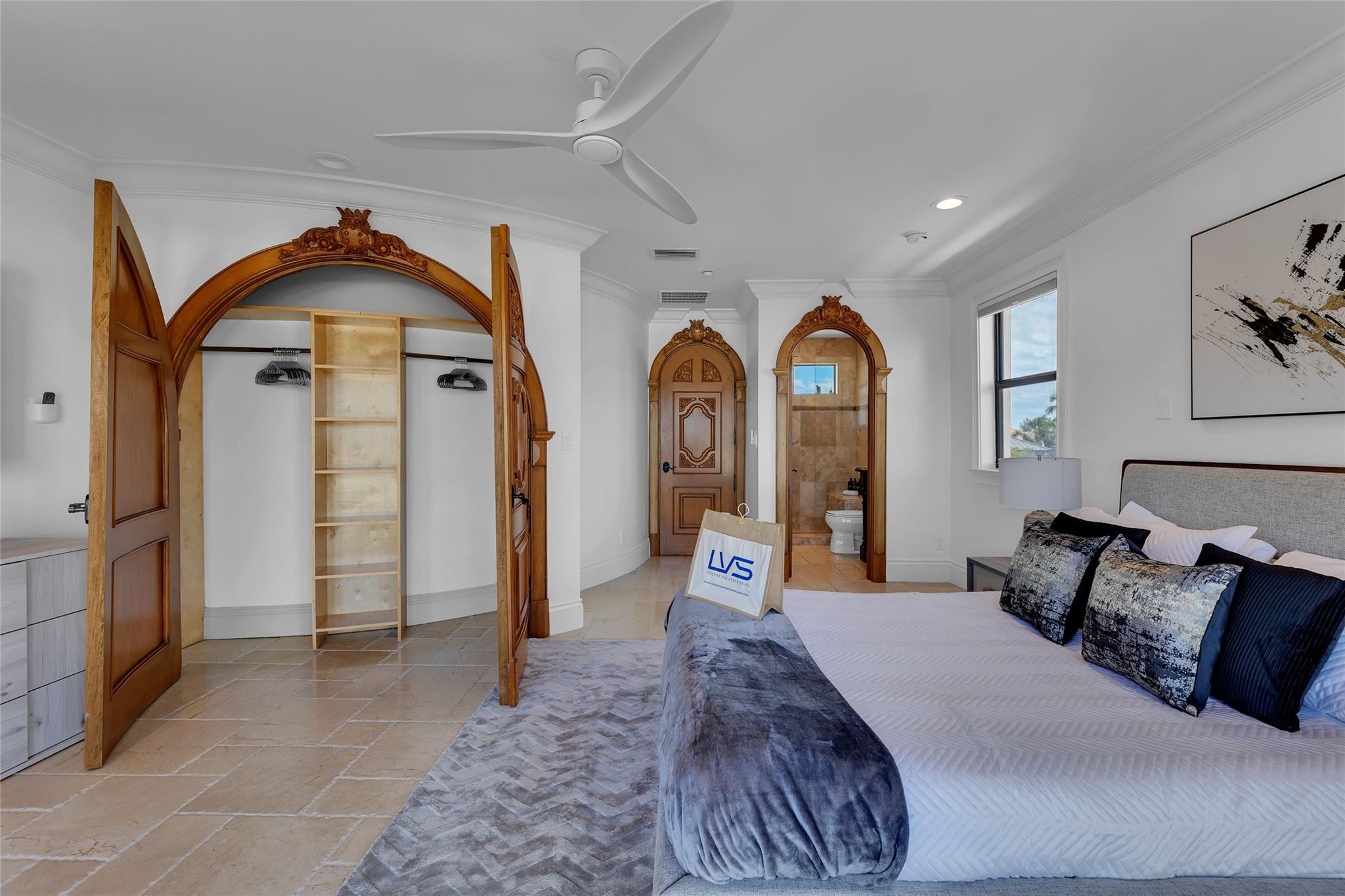 Bedroom with an ornate arched wood closet, tiled floor, and doorway to a bathroom.