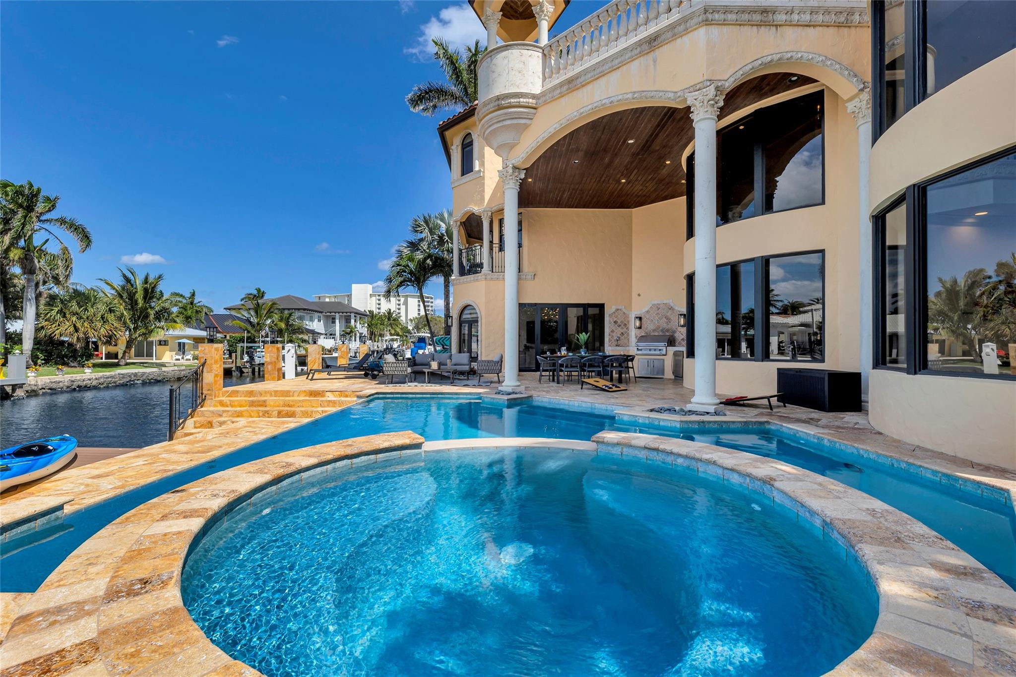 Curved pool beside a Mediterranean-style waterfront home, with arched balconies and a canal dock.