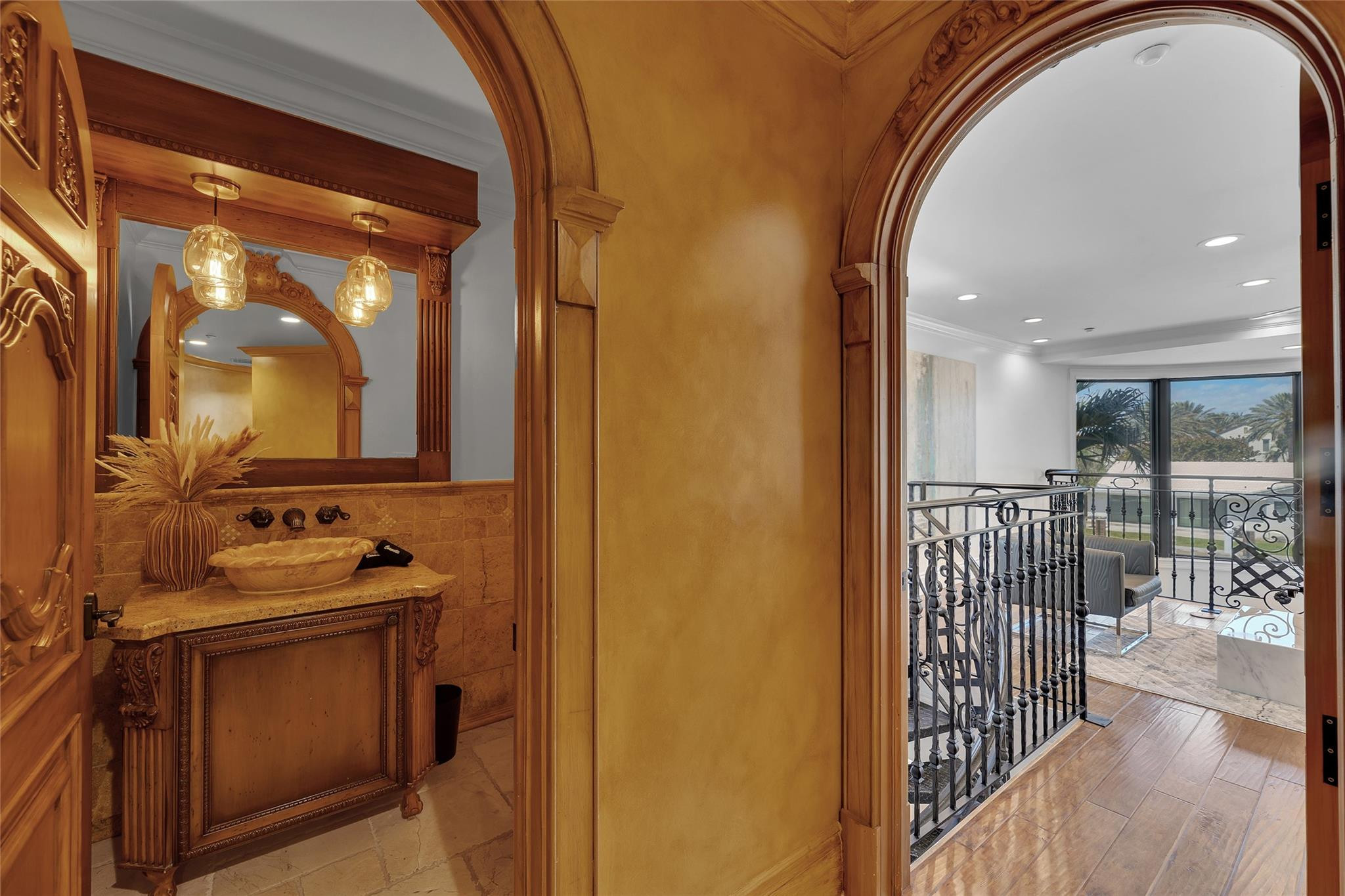 Bathroom vanity beside an ornate archway opening to a bright sitting area with palm views.