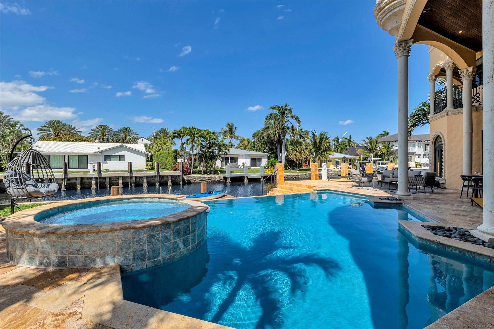 Waterfront home's pool and raised circular spa beside a columned patio and canal dock.