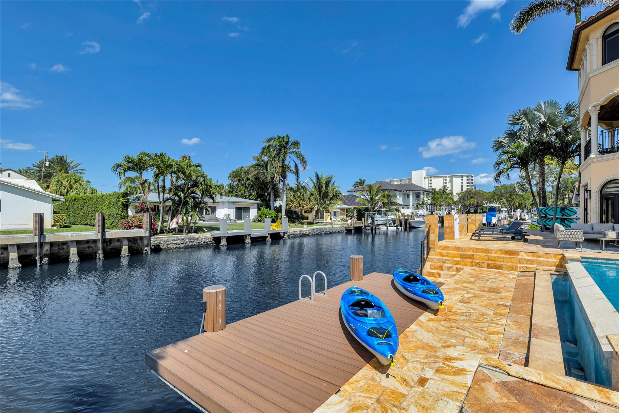 Waterfront patio with a private dock, two blue kayaks, and a pool beside a palm-lined canal.