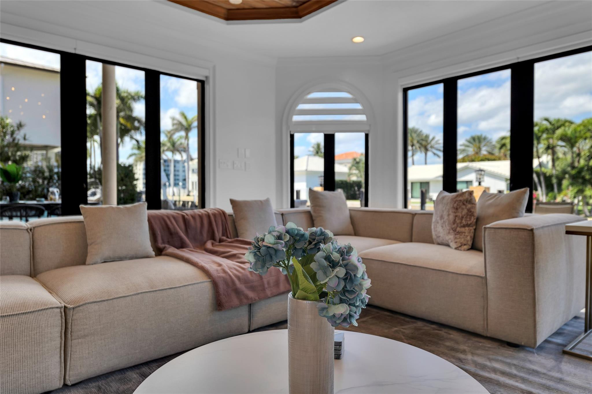 Living room with a beige sectional and arched window overlooking palm trees.