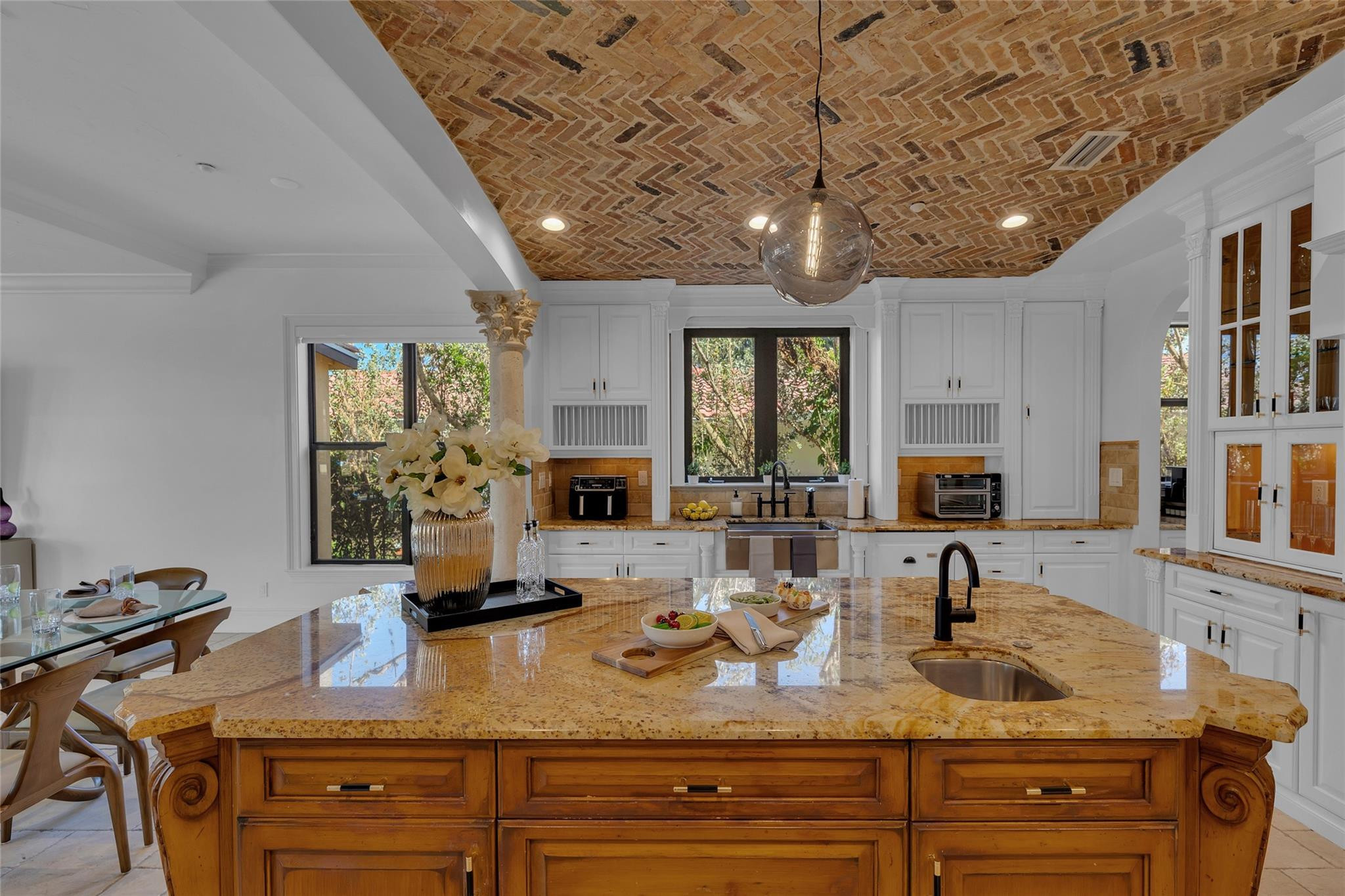 Kitchen with a large stone island, white cabinetry, and an exposed brick ceiling.
