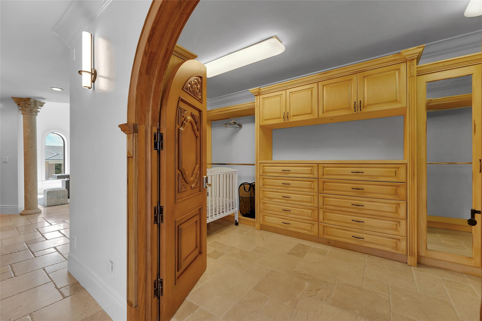 Walk-in closet with honey-colored built-ins, mirrored doors, and an ornate arched wooden entry.
