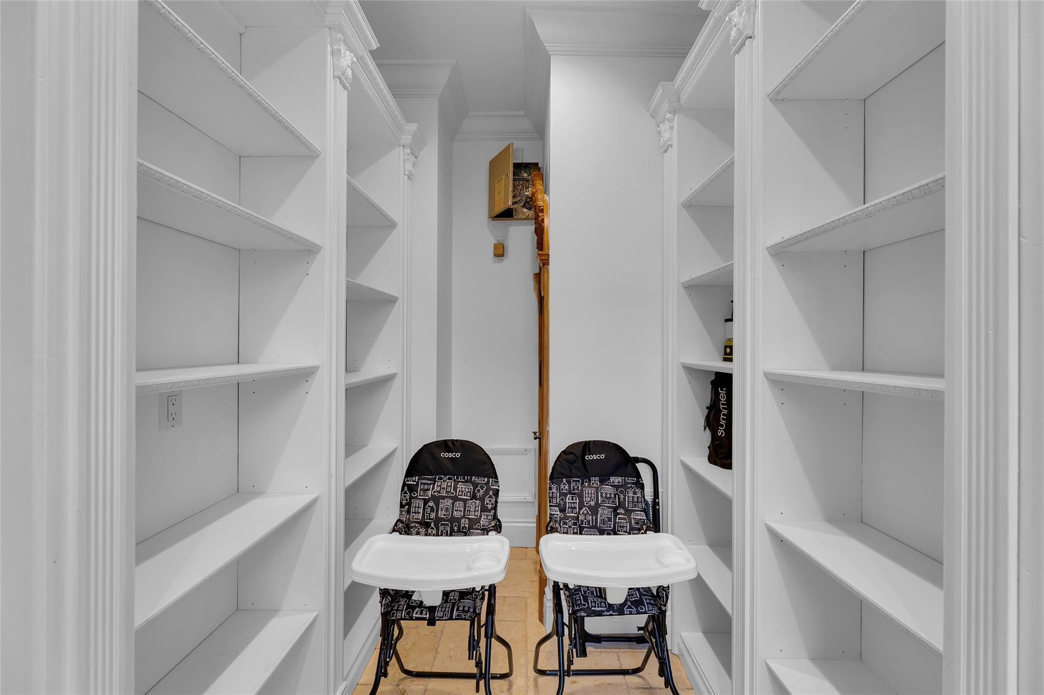 Narrow storage room with built-in shelves and two folding high chairs.