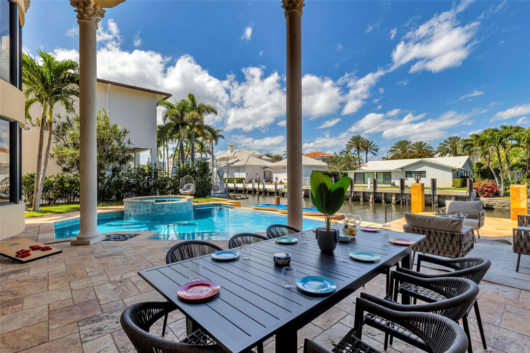 Waterfront patio with a pool, canal dock, and outdoor dining and lounge furniture.