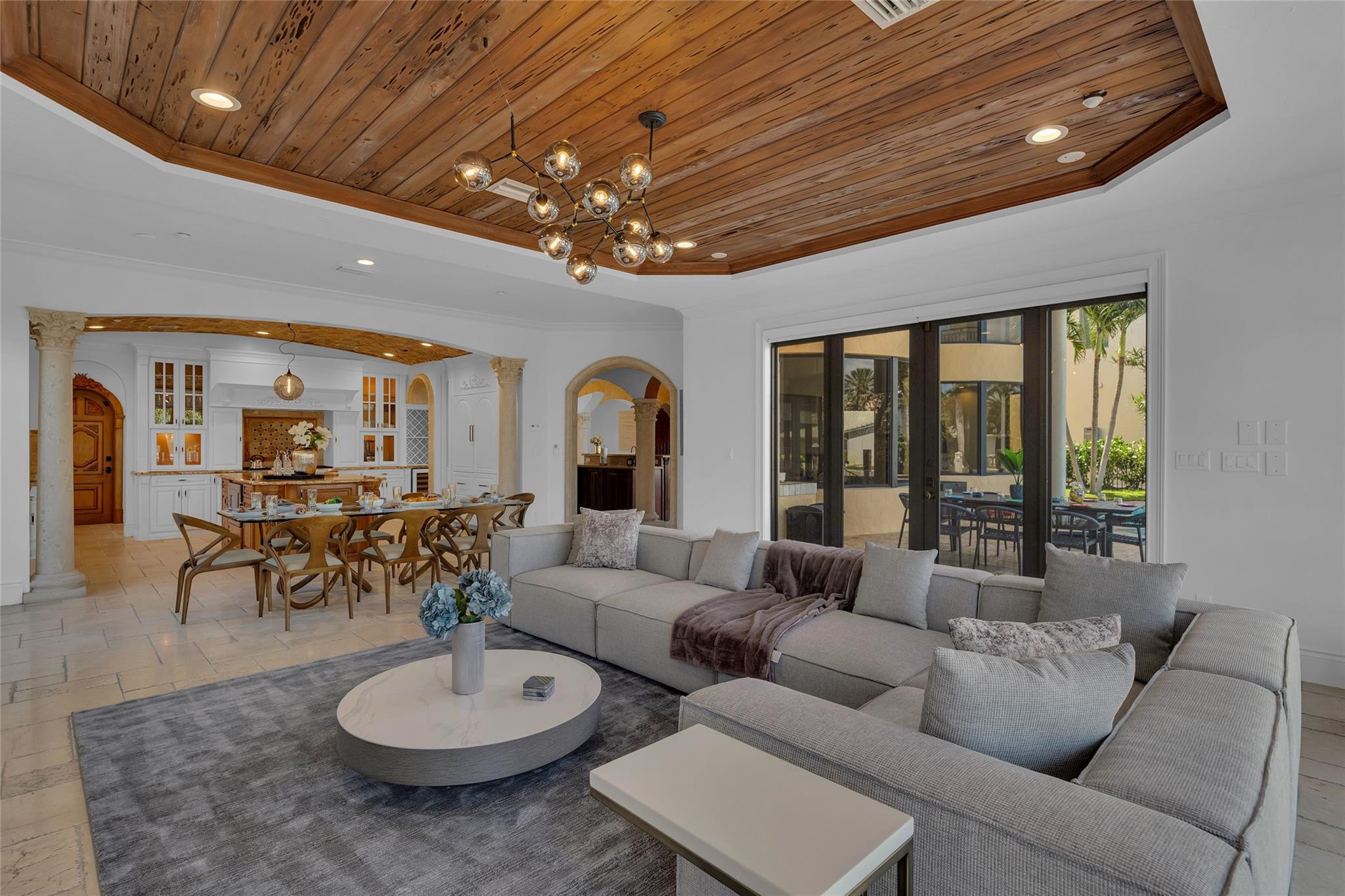 Open-plan living and dining room with a wood-plank ceiling, gray sectional, and sliding doors to the patio.