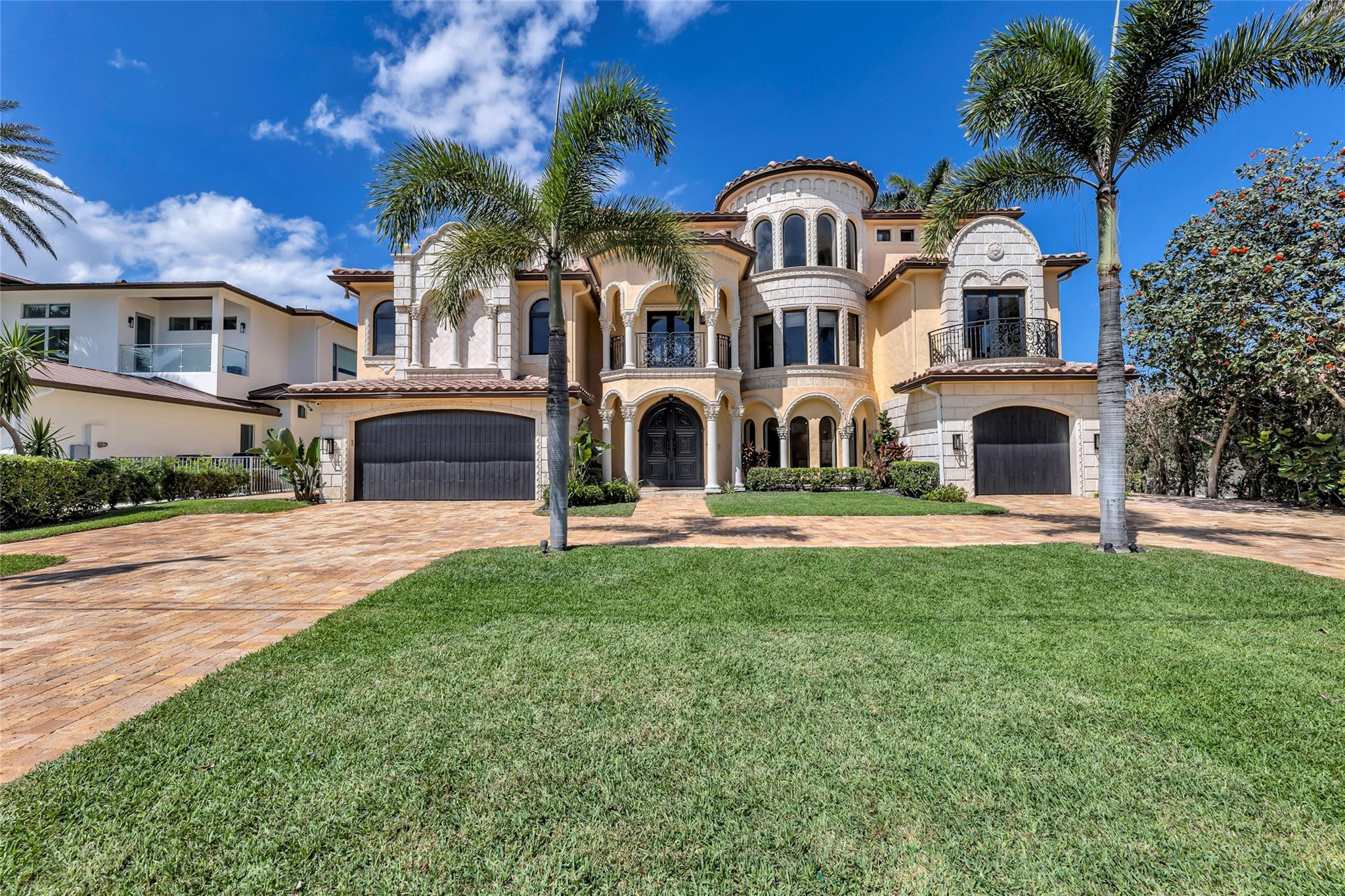 Mediterranean-style home with arched entryways, two garages, palm trees, and a broad paved driveway.