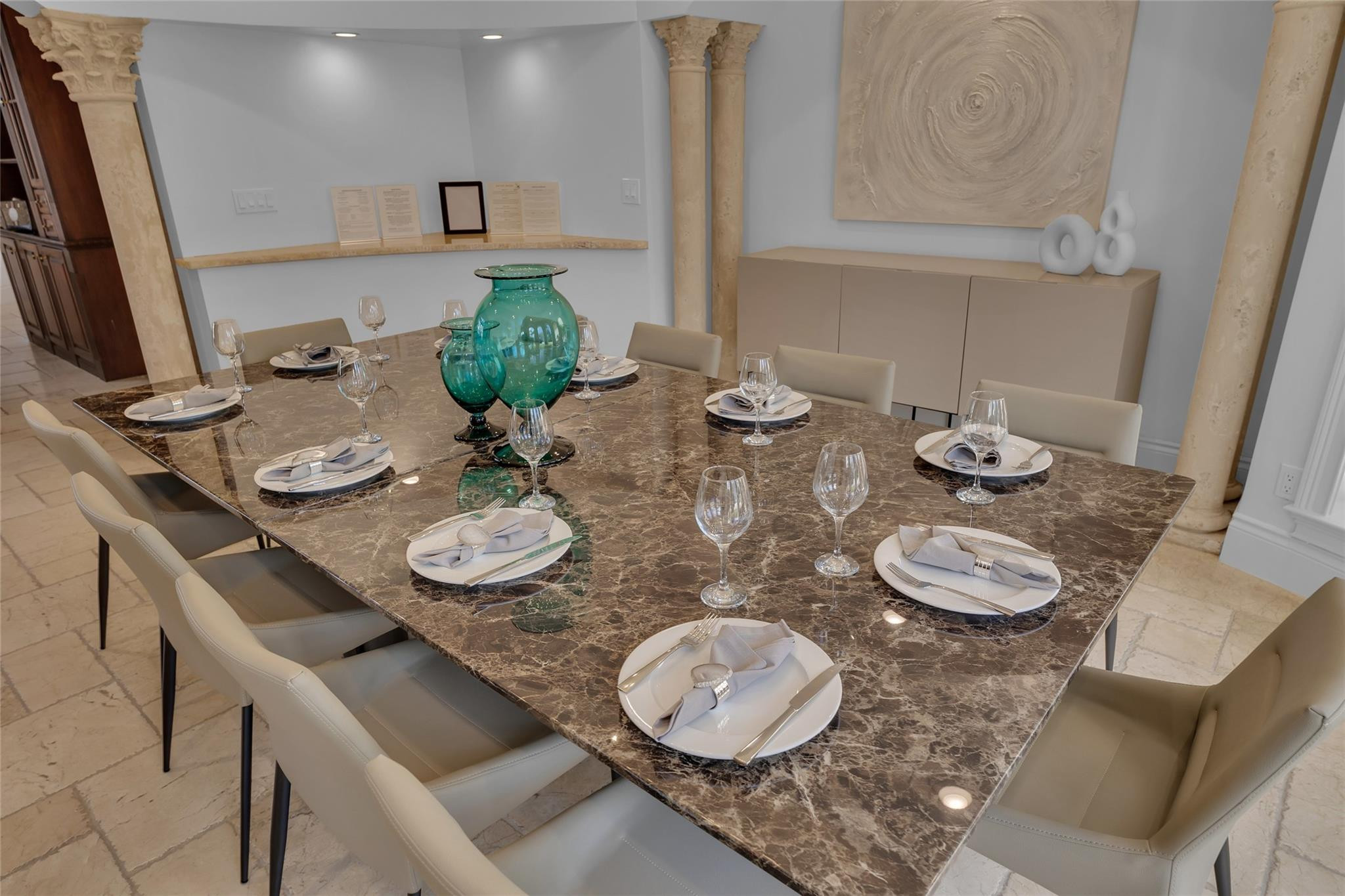 Dining room with a set marble table, cream chairs, and turquoise glass vases at the center.
