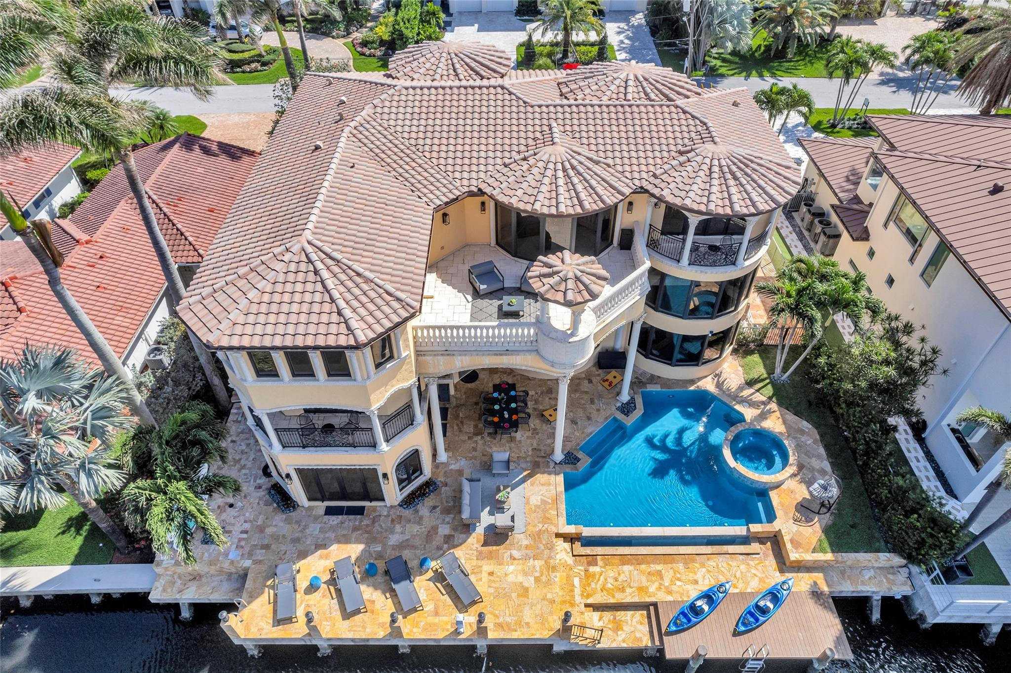 Waterfront home with a pool, circular spa, stone patio, and dock with two kayaks.