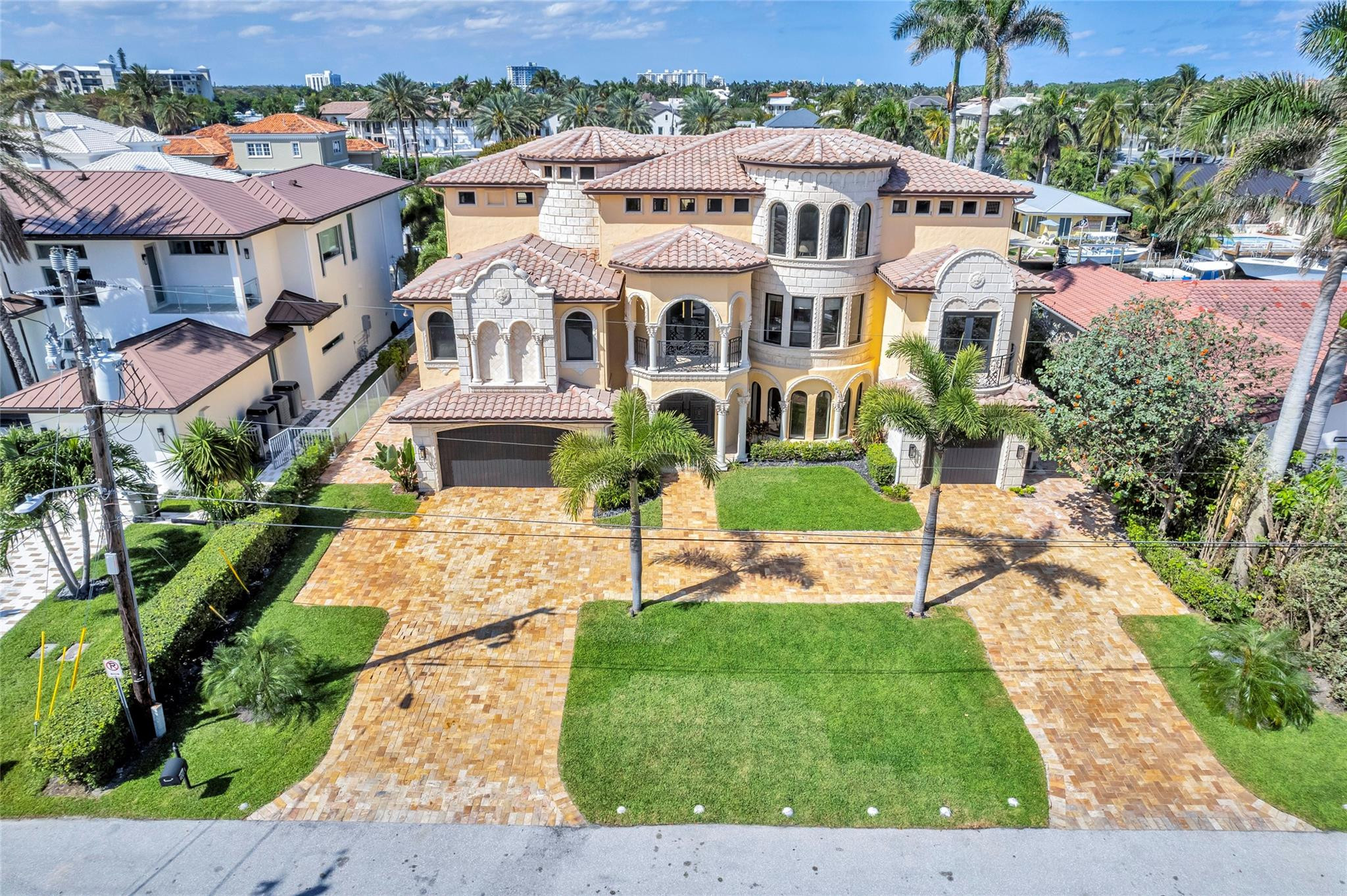 Aerial view of a Mediterranean-style home with arched windows, tile roofs, palms, and a broad paver driveway.