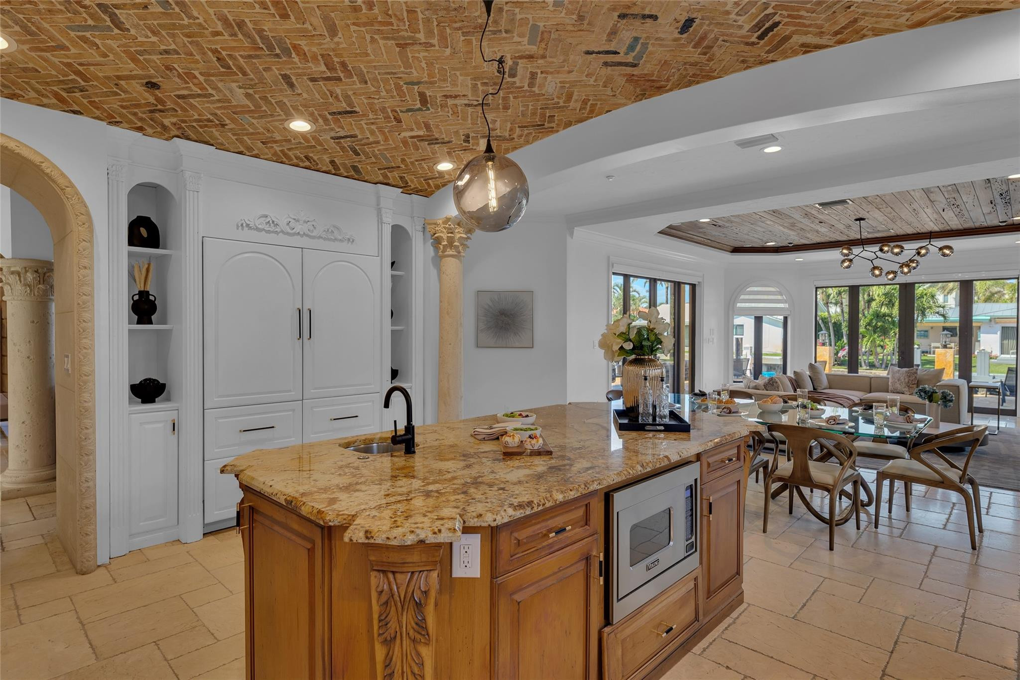 Kitchen with a carved wood island, exposed brick ceiling, and open dining and living areas.