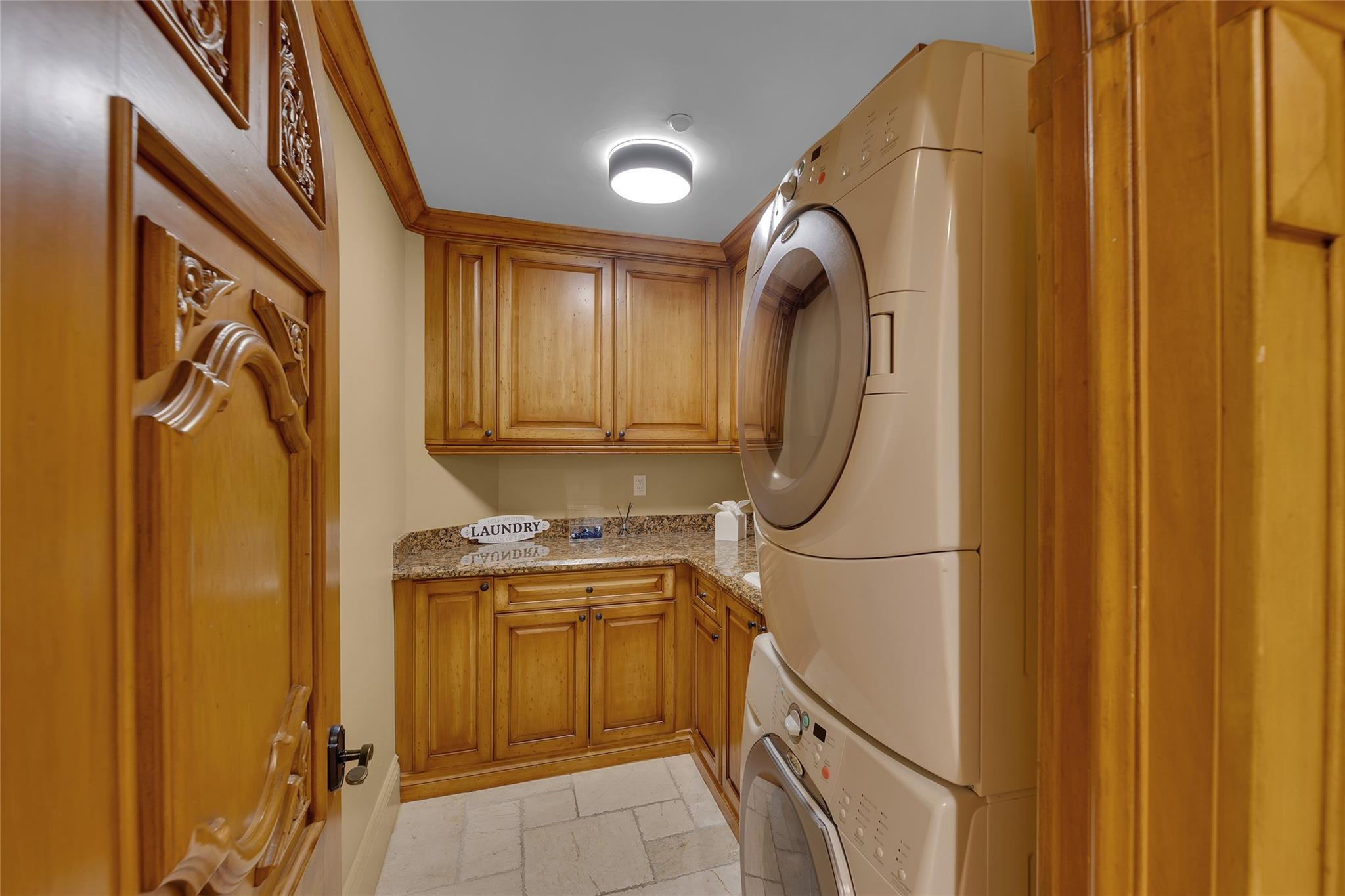 Laundry room with stacked washer and dryer, wood cabinetry, and granite counters.