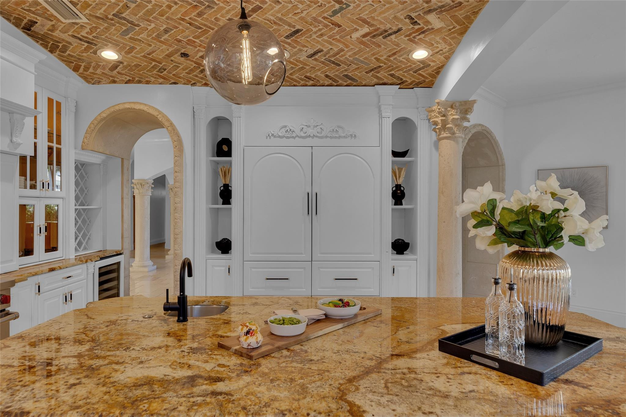White kitchen with a golden stone island, brick ceiling, and ornate arched openings.