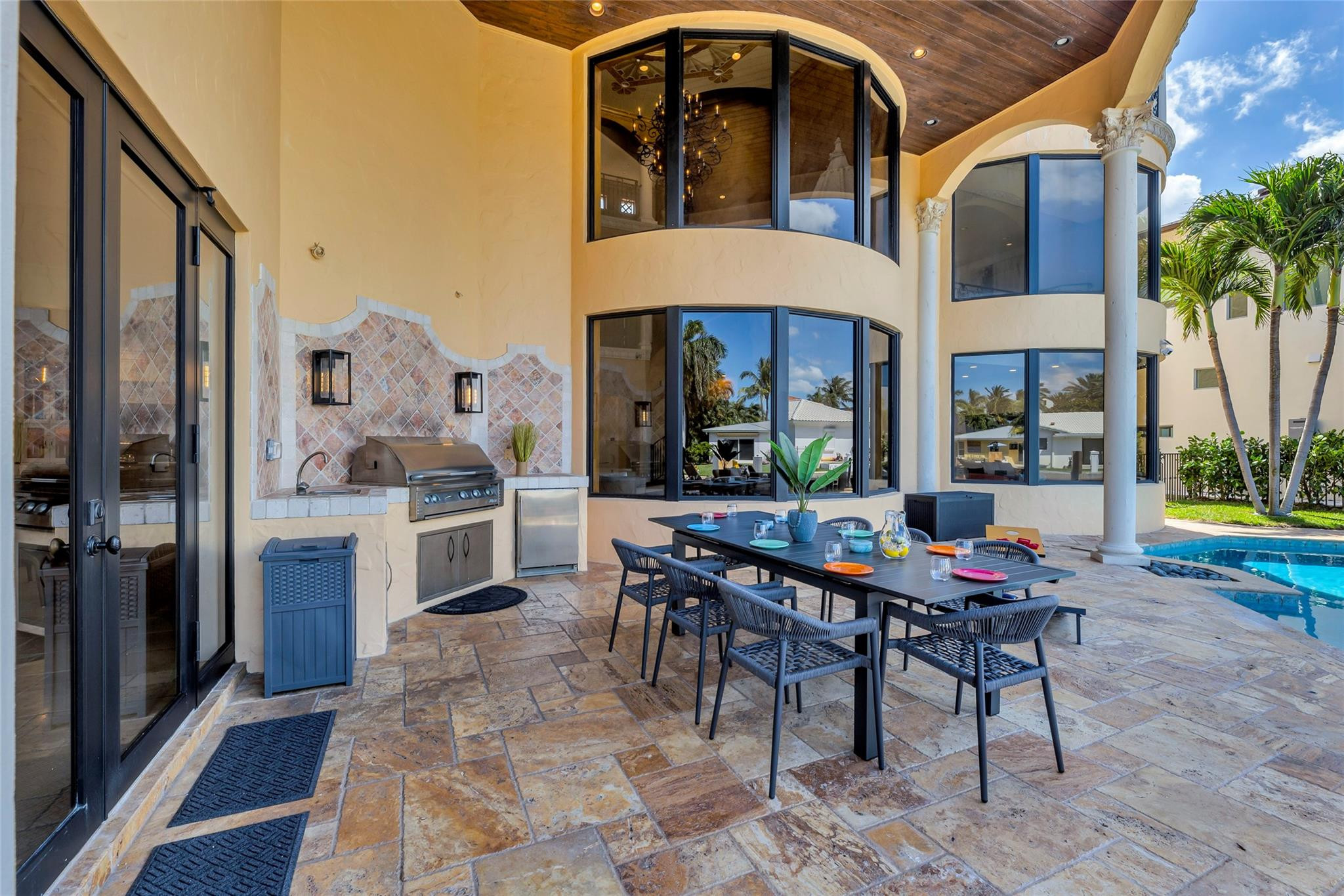 Covered patio with an outdoor kitchen, set dining table, and swimming pool.