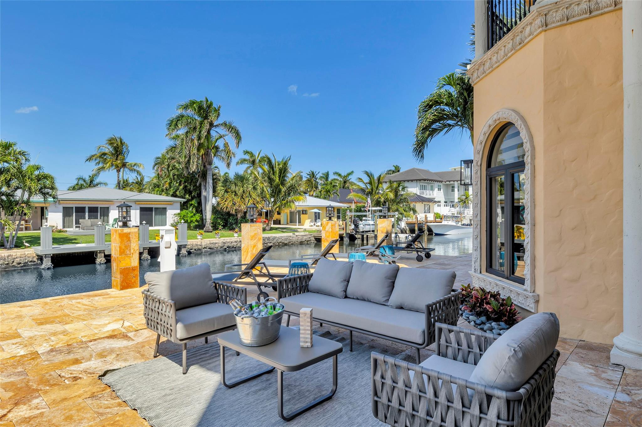Waterfront patio with gray lounge seating beside a palm-lined canal.