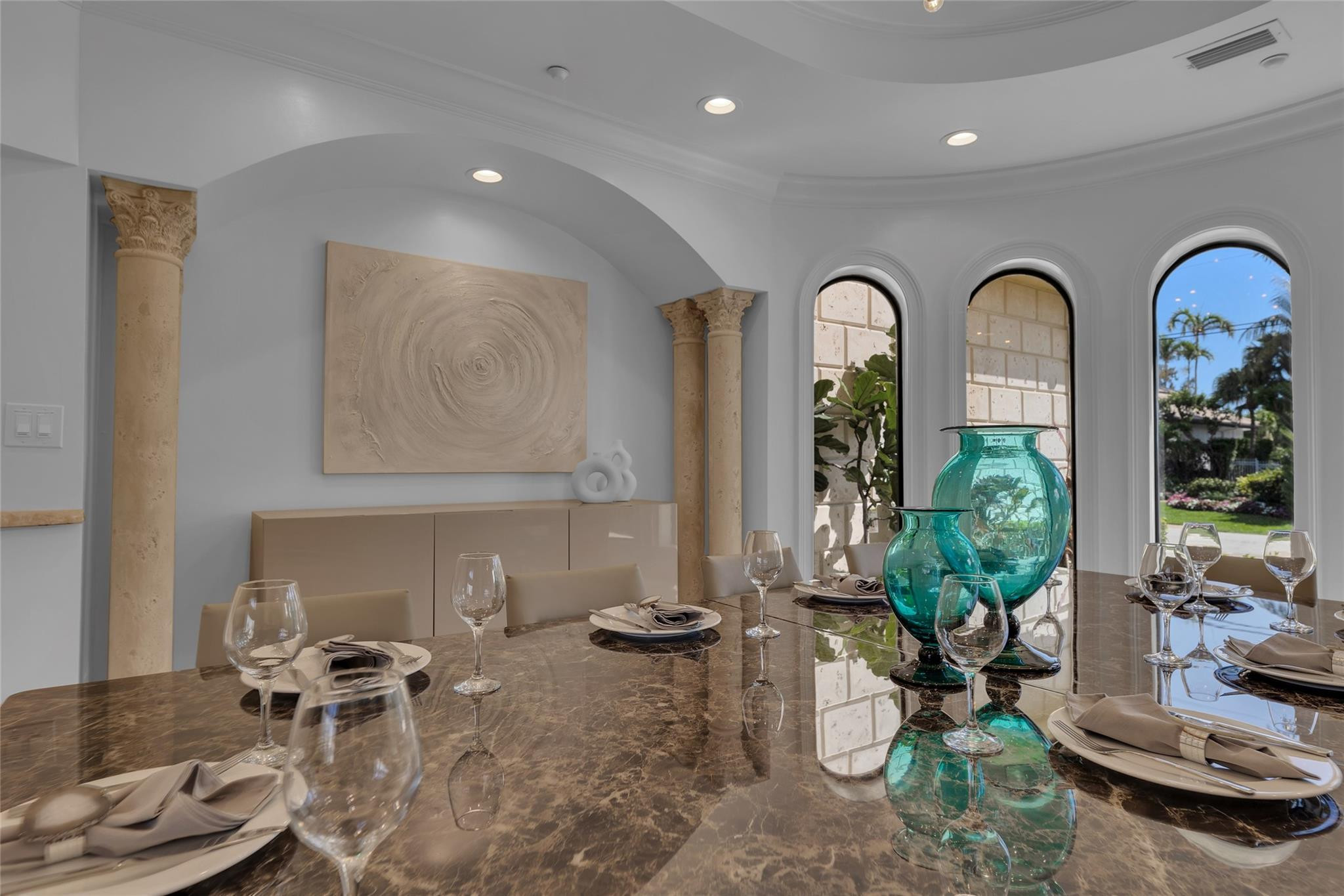 Dining room with a set marble table, turquoise glass vases, arched windows, and stone columns.