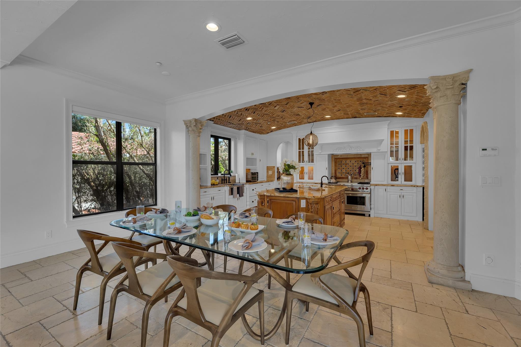 Dining area and kitchen with a set glass table, carved wood island, and brick-vaulted ceiling.