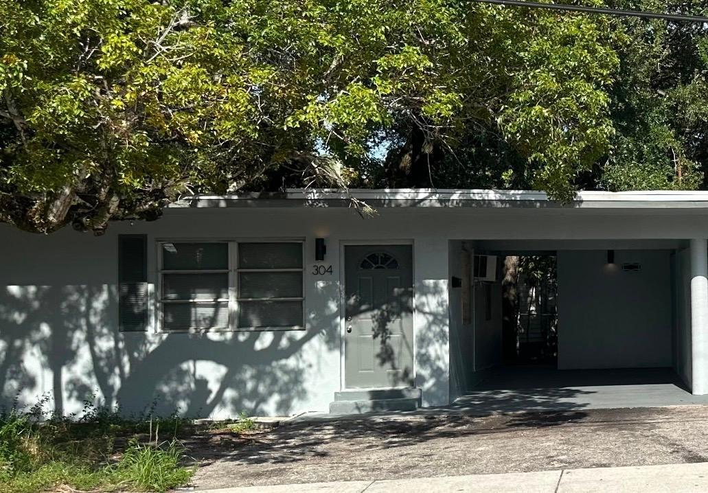 Single-story home with an open carport, shaded by a large leafy tree.