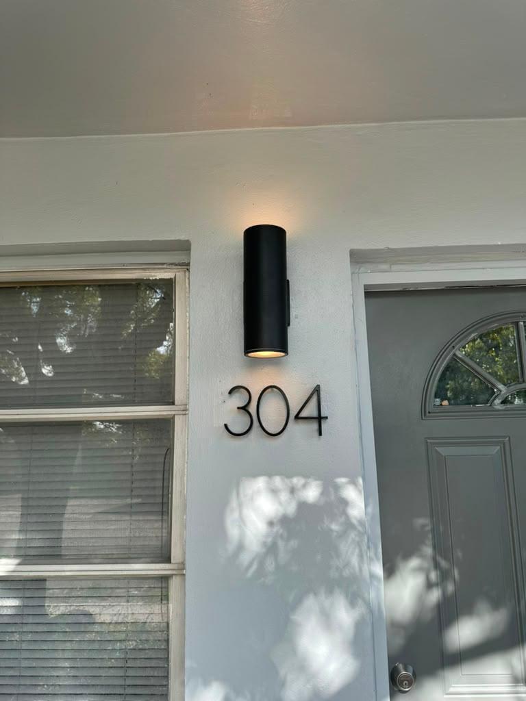 Home entrance with the number 304, a black wall sconce, gray door, and window with blinds.
