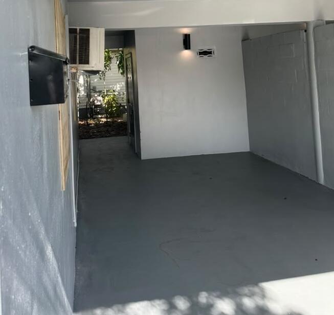Vacant garage with a gray concrete floor and an open rear entrance facing greenery.