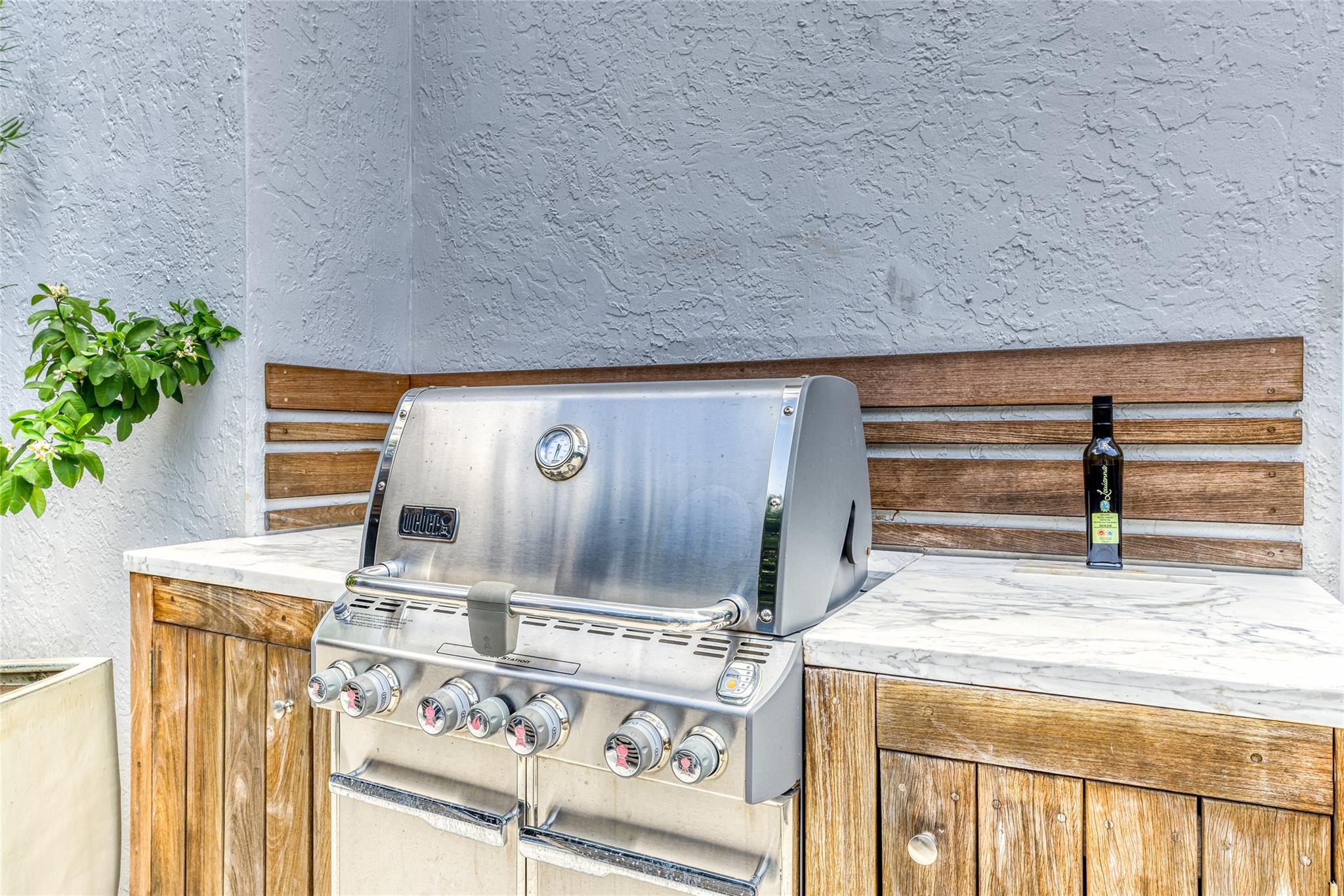 Outdoor kitchen with a stainless-steel grill, wooden cabinetry, and white marble countertops.