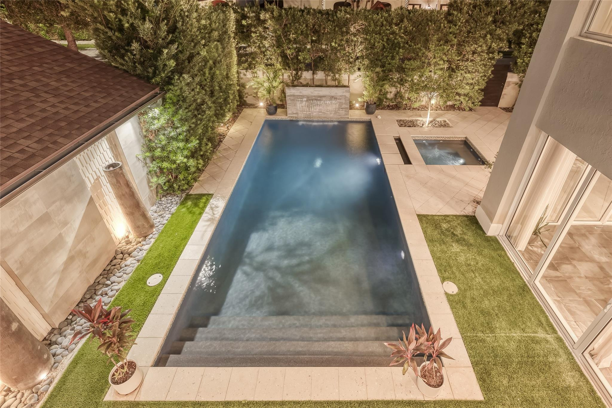 Rectangular swimming pool and raised spa in a landscaped courtyard at night.