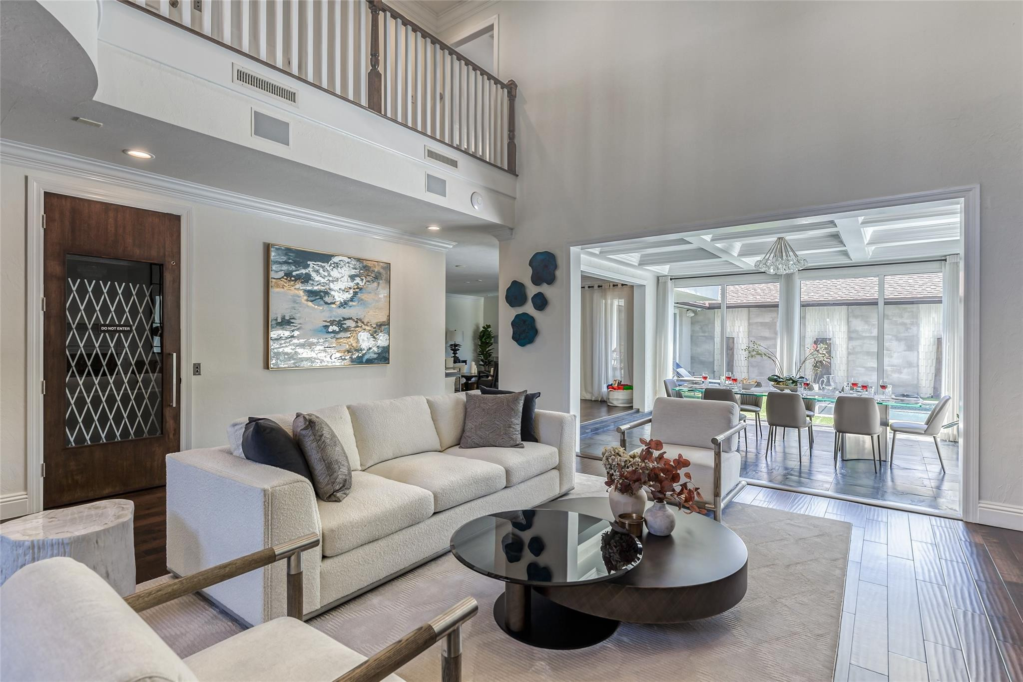 Living room with a white sofa and loft balcony opening to a bright dining area with large windows.