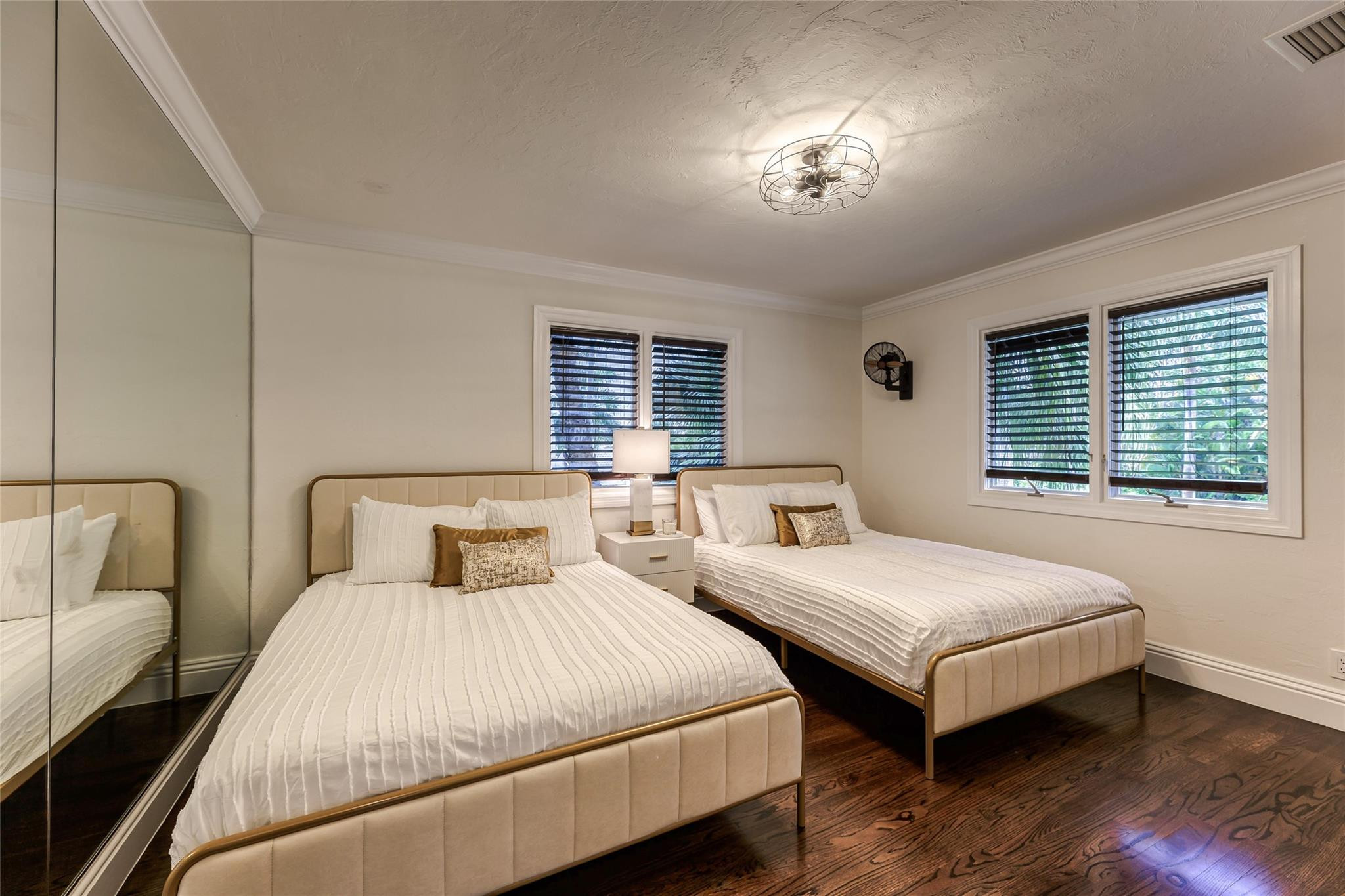 Bedroom with two cream beds, mirrored closet doors, and dark hardwood floors.