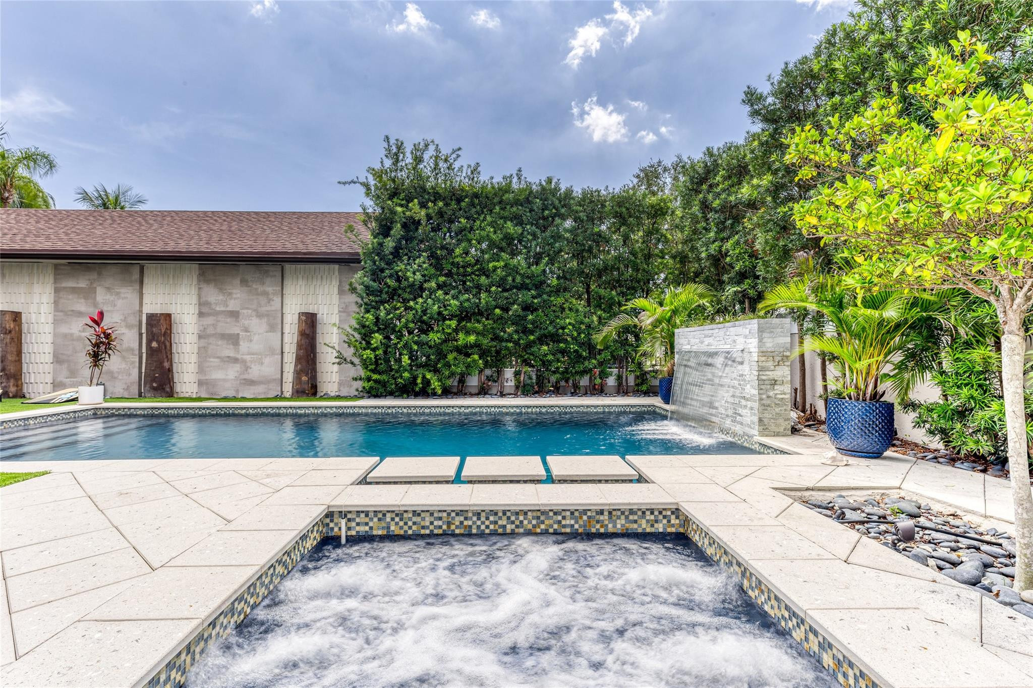 Swimming pool and bubbling spa with a stone waterfall and tropical landscaping.