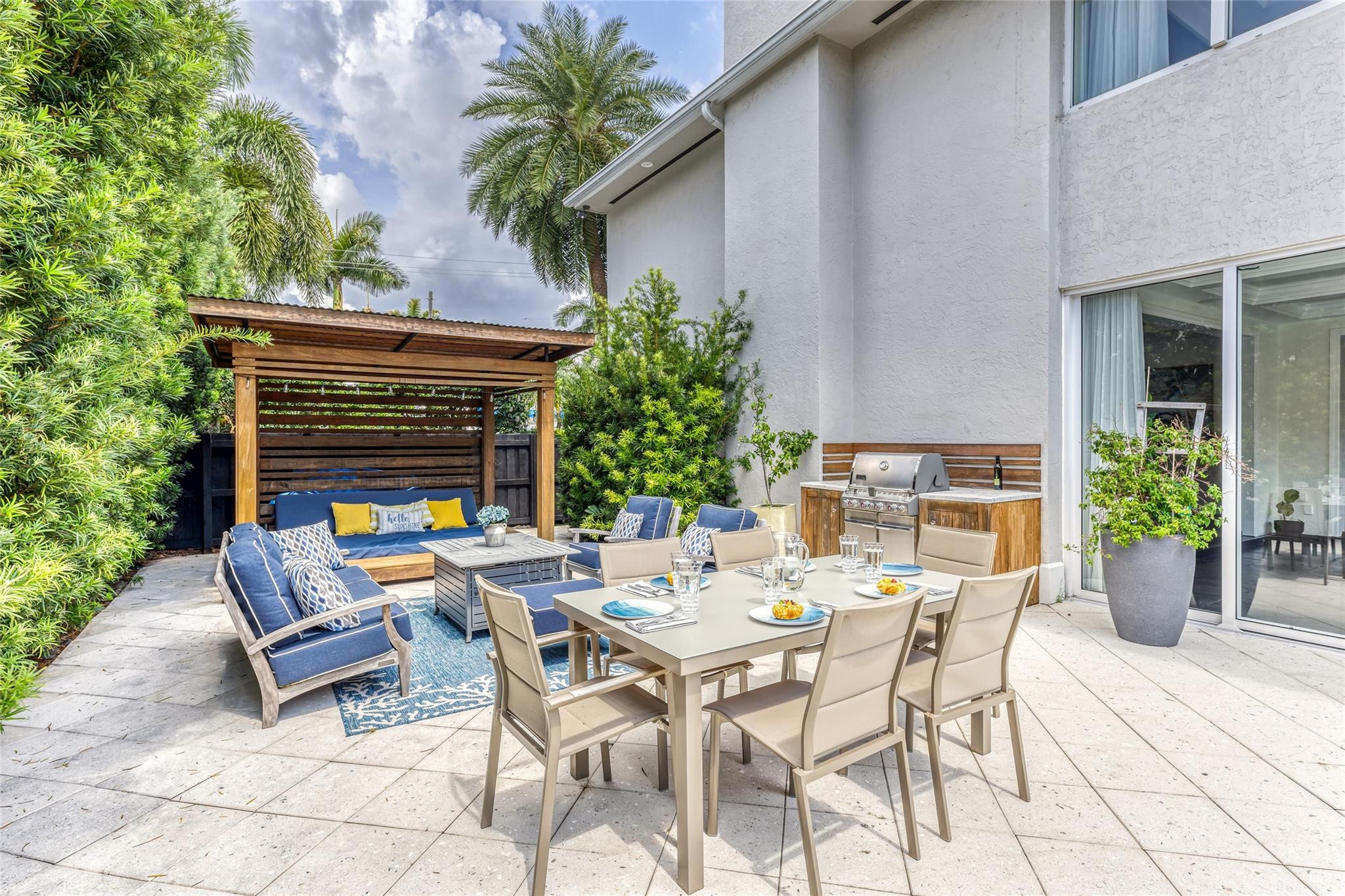 Patio with a set dining table, stainless steel grill, and pergola-covered blue lounge seating.