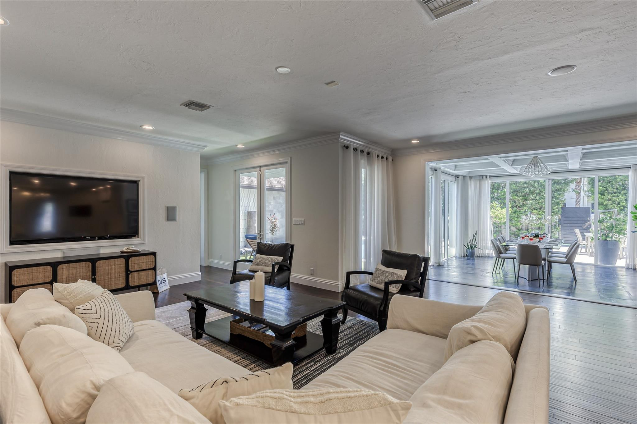 Living room with cream sofas and black armchairs opens into a dining area through wide glass doors.