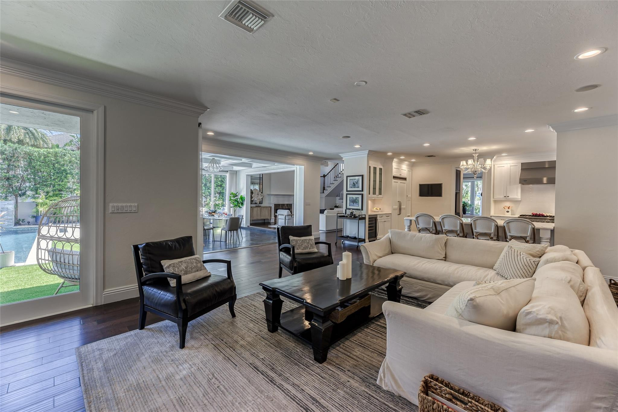 Open-plan living room with cream sofas, black chairs, and views toward the kitchen and backyard pool.