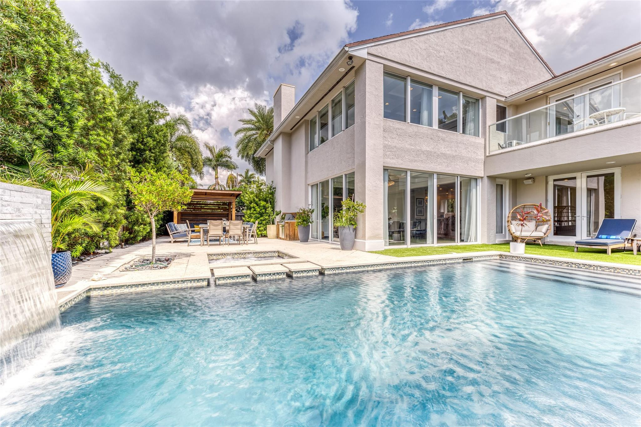 Modern two-story home beside a swimming pool with a waterfall and furnished patio.