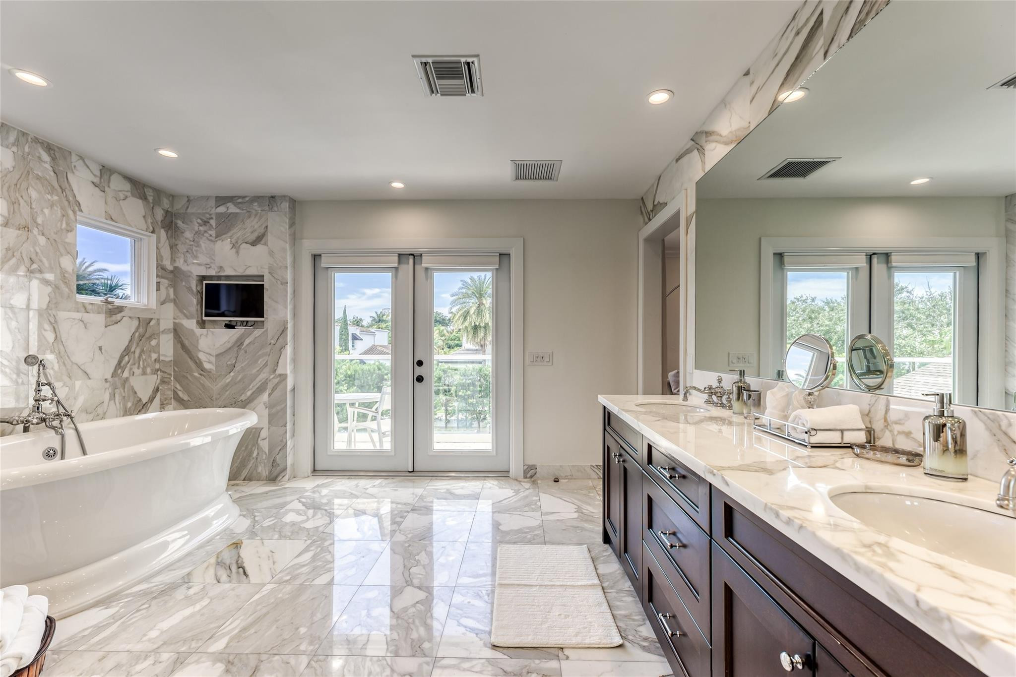 Marble bathroom with a freestanding tub, dark double vanity, and glass doors opening to a balcony.