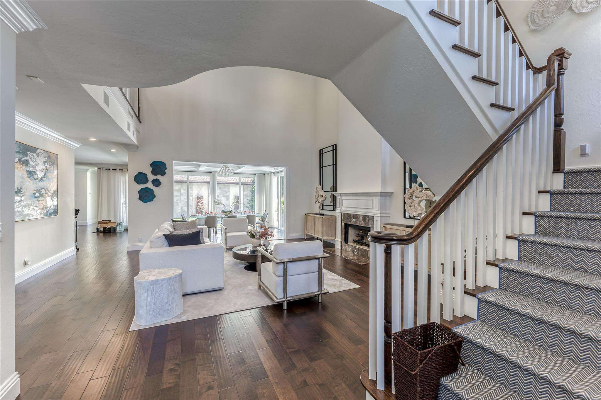 Living room with a fireplace, white seating, dark wood floors, and a carpeted staircase.