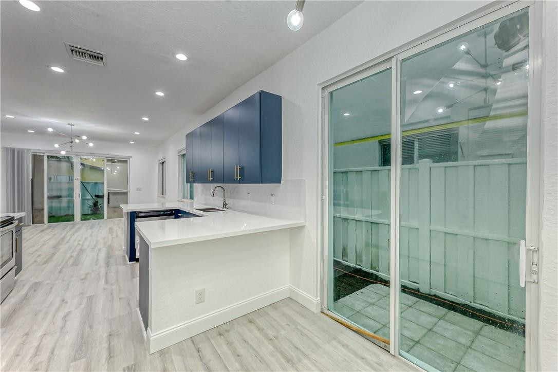 Vacant kitchen with navy cabinets, white peninsula, and sliding glass doors to a fenced patio.