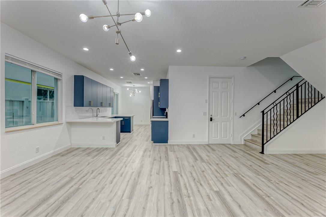 Open-plan living area with blue kitchen cabinets, gray plank flooring, and a black-railed staircase.