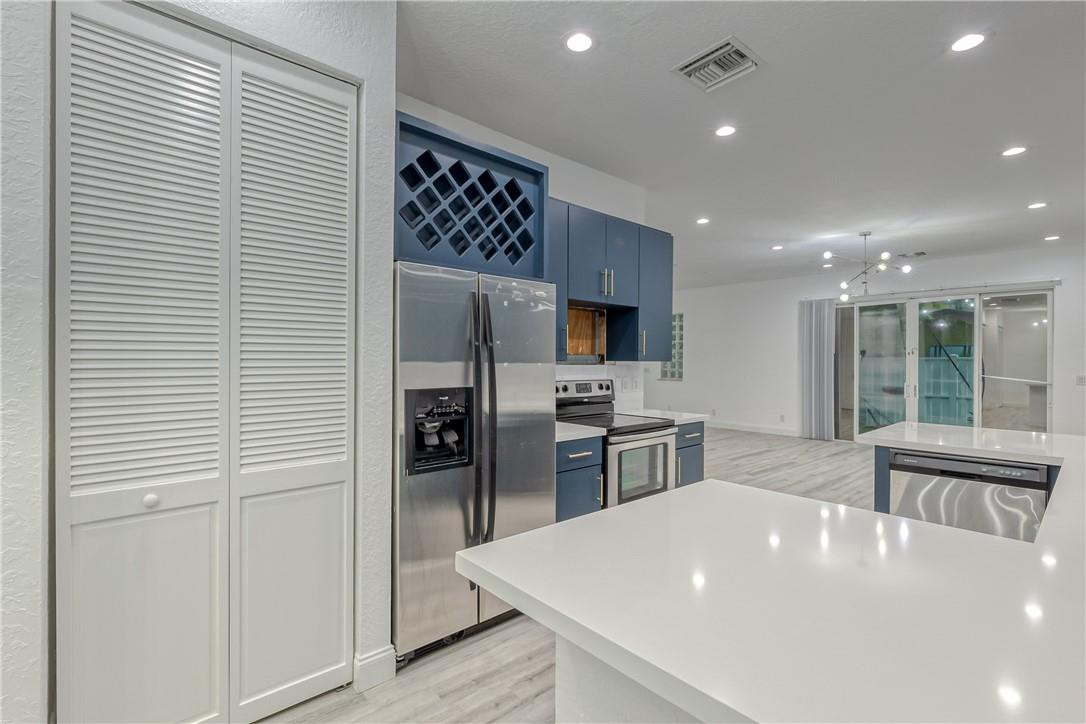 Open kitchen with blue cabinets, stainless appliances, a built-in wine rack, and a large white island.