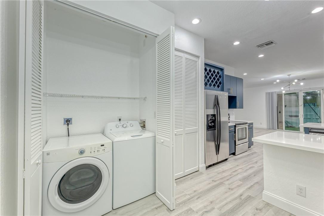Laundry area with washer and dryer beside a blue-and-white kitchen with stainless steel appliances.